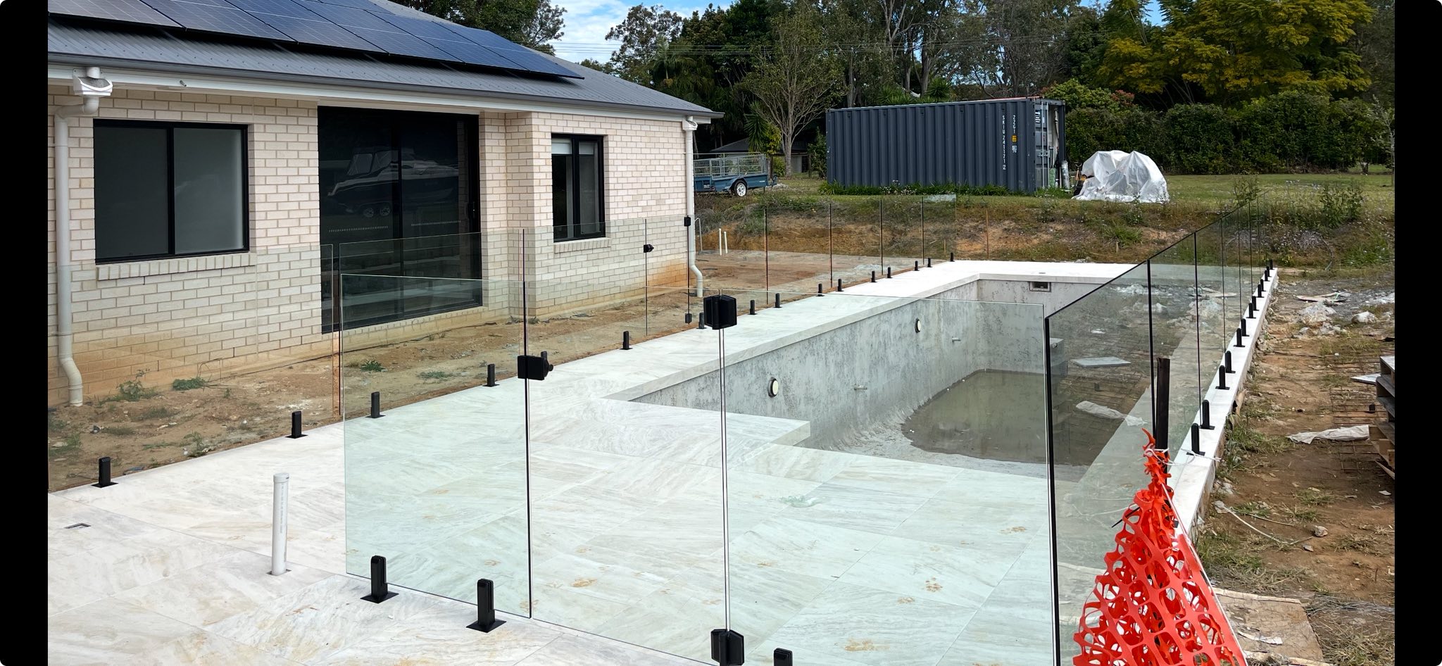 Frameless glass pool fence with black spigots on a new build
